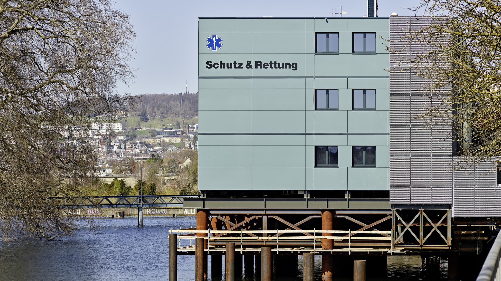 Limmatprovisorium, Zürich - Seitenansicht eines zweigeschossigen Holzmodulbaus auf einer Stahlbau Pfählung über dem Limmat Fluss