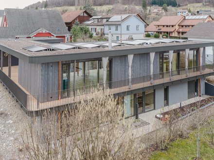 Das Einfamilienhaus präsentiert sich als moderner, terrassierter Baukörper mit grosszügigen Verglasungen und klarer Flachdacharchitektur. Die filigrane Pfosten-Riegel-Fassade prägt das Erscheinungsbild des Obergeschosses und öffnet die Wohnräume zur Umgebung hin. Weit auskragende Dachflächen schützen die Fassadenbereiche und unterstreichen die horizontale Gliederung des Gebäudes. Durch die erhöhte Hanglage entstehen attraktive Ausblicke auf die umliegende Landschaft und die Nachbarbebauung. Die Kombination aus transparenter Fassadenkonstruktion, klaren Linien und zurückhaltender Materialisierung verleiht dem Gebäude eine zeitgemässe und elegante Erscheinung. Das Einfamilienhaus präsentiert sich als moderner, terrassierter Baukörper mit grosszügigen Verglasungen und klarer Flachdacharchitektur. Die filigrane Pfosten-Riegel-Fassade prägt das Erscheinungsbild des Obergeschosses und öffnet die Wohnräume zur Umgebung hin. Weit auskragende Dachflächen schützen die Fassadenbereiche und unterstreichen die horizontale Gliederung des Gebäudes. Durch die erhöhte Hanglage entstehen attraktive Ausblicke auf die umliegende Landschaft und die Nachbarbebauung. Die Kombination aus transparenter Fassadenkonstruktion, klaren Linien und zurückhaltender Materialisierung verleiht dem Gebäude eine zeitgemässe und elegante Erscheinung.