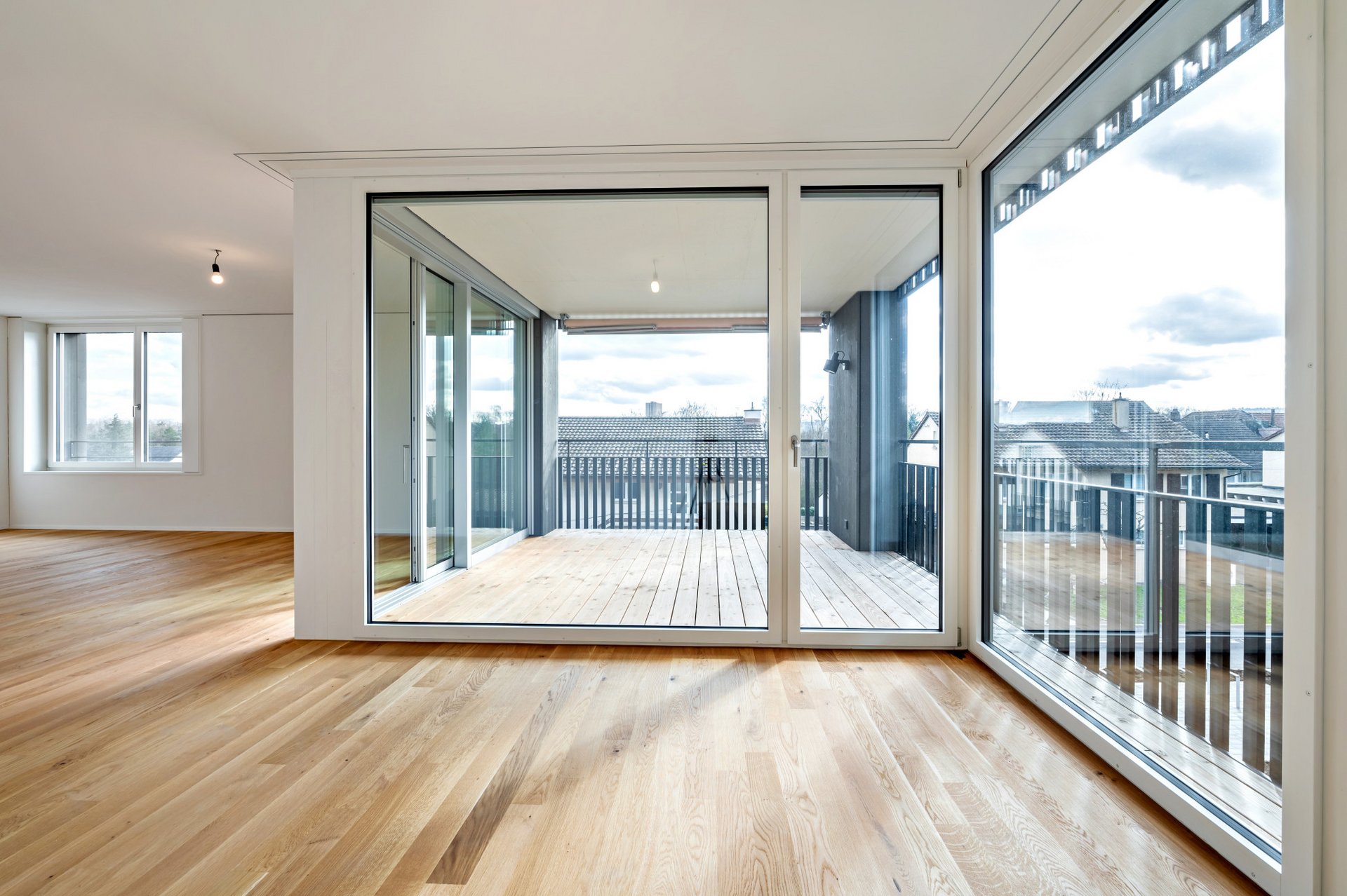 Innenansicht durch ein grossflächiges Fenster auf den Balkon, helle Wände und heller Holzboden 