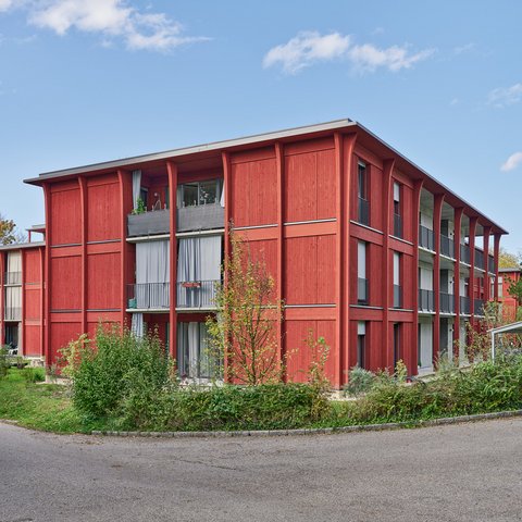 Hirtenweg, Riehen - Aussenansicht der gesamten Anlage mit drei Wohngebäuden all in leuchtendem rot in grüner, blühender Parkanlage 