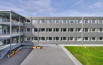 Frontale Ansicht auf das Gebäude, mit Aussenanlage. 