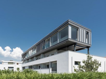 Wohnungsaufstockung, Bournoud - Eckansicht Vorderseite mit in Grautönen gehaltener Fassade und raumhohen Fenstern 