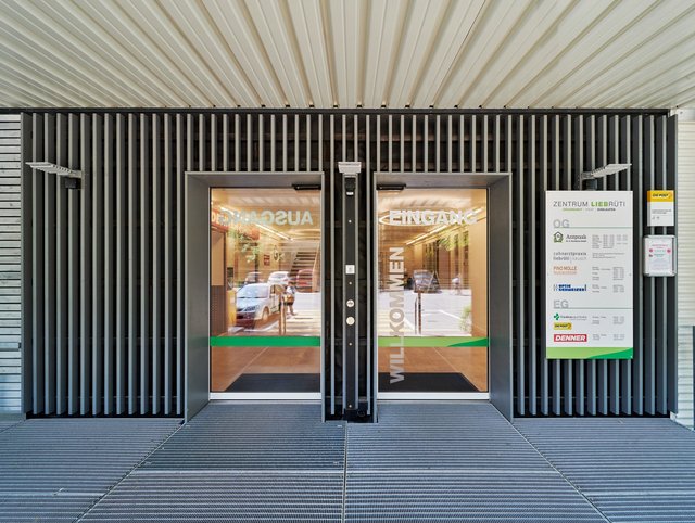 Einkaufszentrum Liebrüti, Kaiseraugst - Nahaufnahme des überdachten Eingangs mit automatischer Tür und dunkler Fassade