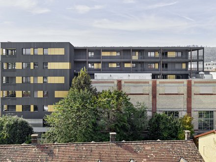 Lokwerk, Winterthur - Aussenansicht frontal auf bestehendes Gebäude mit Backsteinfassade und Aufstockung mit dunkler Fassade und gelben Akzenten Lokwerk, Winterthur - Aussenansicht frontal auf bestehendes Gebäude mit Backsteinfassade und Aufstockung mit dunkler Fassade und gelben Akzenten