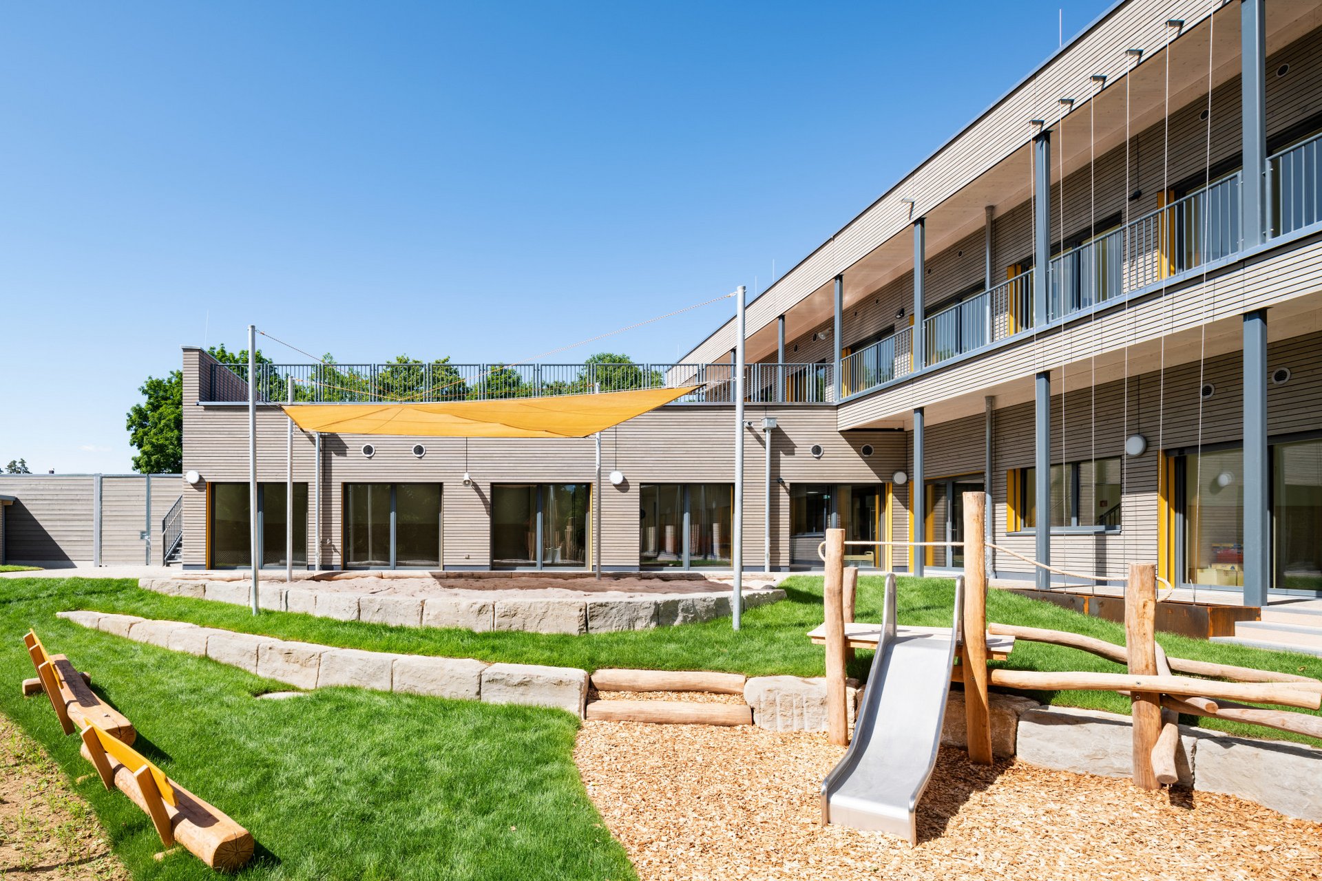 Aussenansicht des Gebäudes mit Holzfassade und Spielplatz